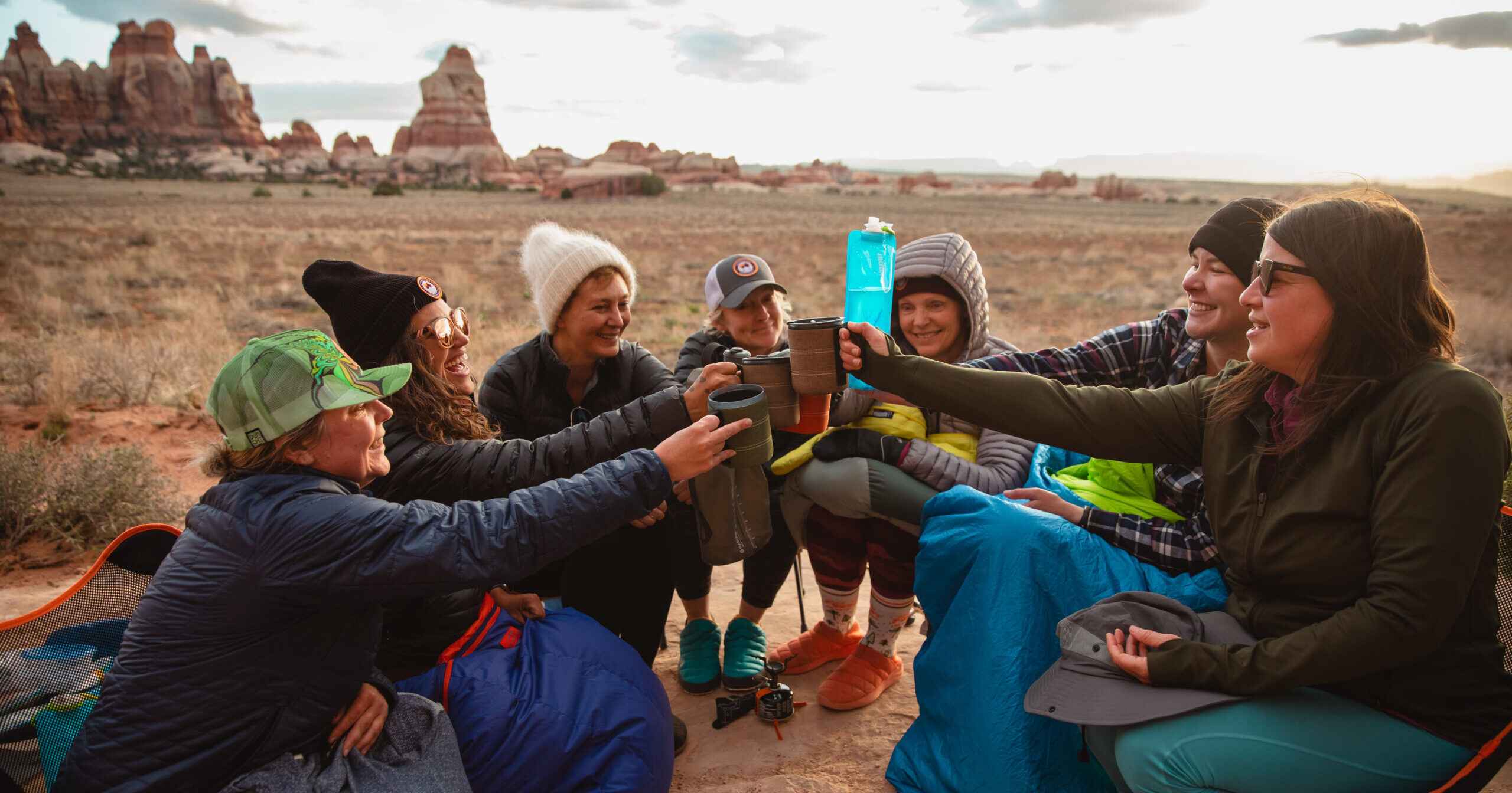 A group of women from the Women's Wine Hiking Society enjoying a toast outdoors with scenic red rock formations in the background.